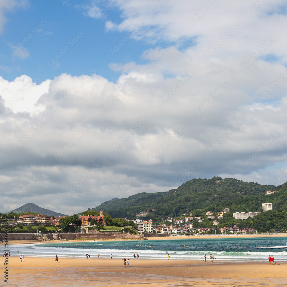 Wide sandy beach with people walking on a sunny day on the ocean coast in the Spanish city of San Sebastian