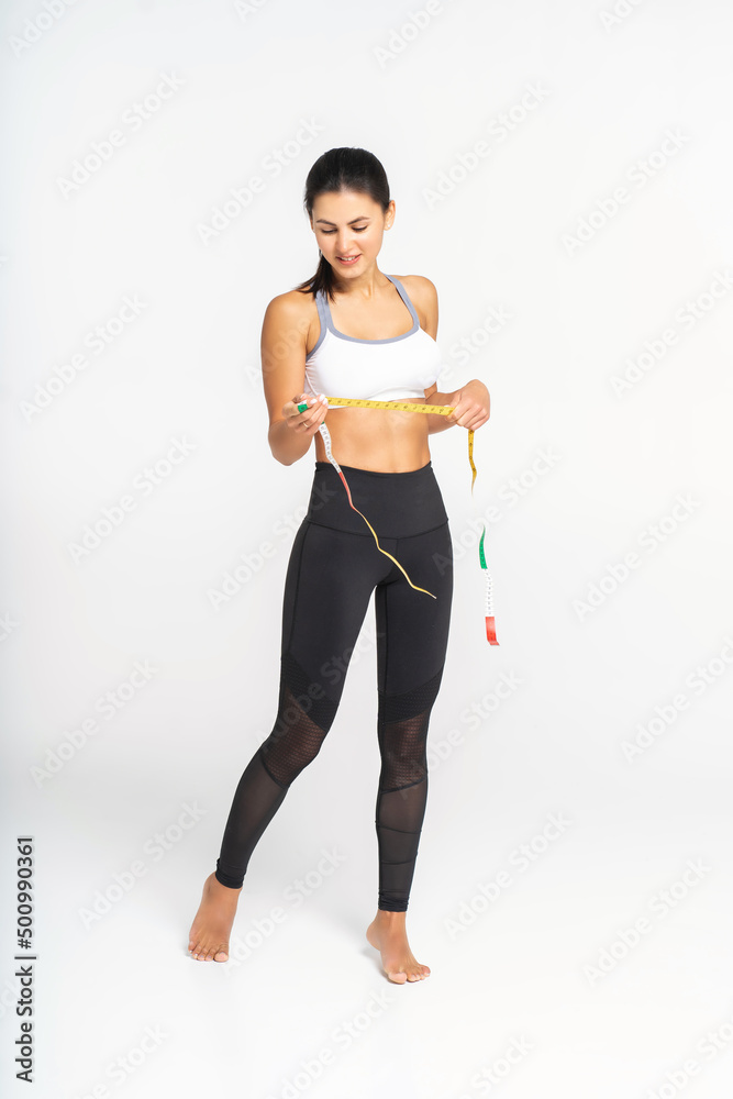 Weight loss, slim body, healthy lifestyle concept. Fitness girl measuring her waistline with measure tape, isolated on white. Copy space. Slim woman measuring her waist Weight loss, slim body, healthy lifestyle concept. Fitness girl measuring her waistline with measure tape, isolated on white. Copy space. Slim woman measuring her waist