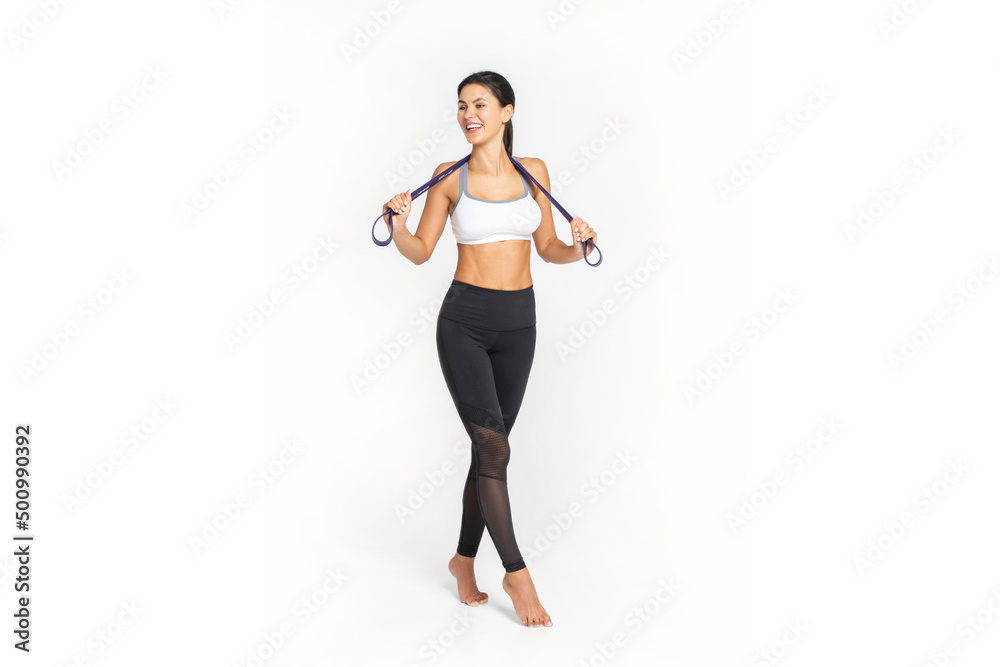 Self determined bodybuilder with rubber band, works on hands and legs, wears comfortable sneakers and sports clothes, poses against white wall. Sport and goals concept. Self determined bodybuilder with rubber band, works on hands and legs, wears comfortable sneakers and sports clothes, poses against white wall. Sport and goals concept.