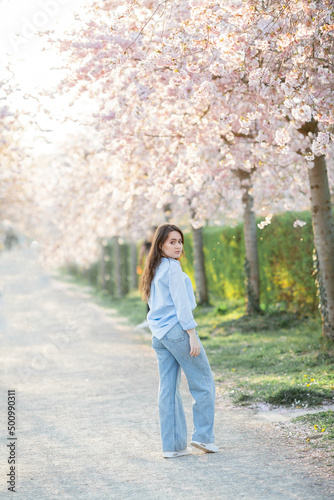 Beautiful young woman of 19 years old in light casual clothes in pastel shades near flowering sakura trees. Spring portrait of model with blue eyes.