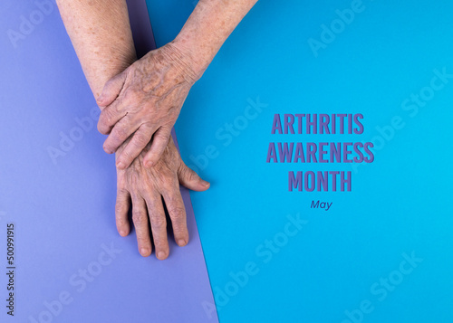 Hands of elderly woman crossed on blue and violet background. Arthritis Awareness Month concept.