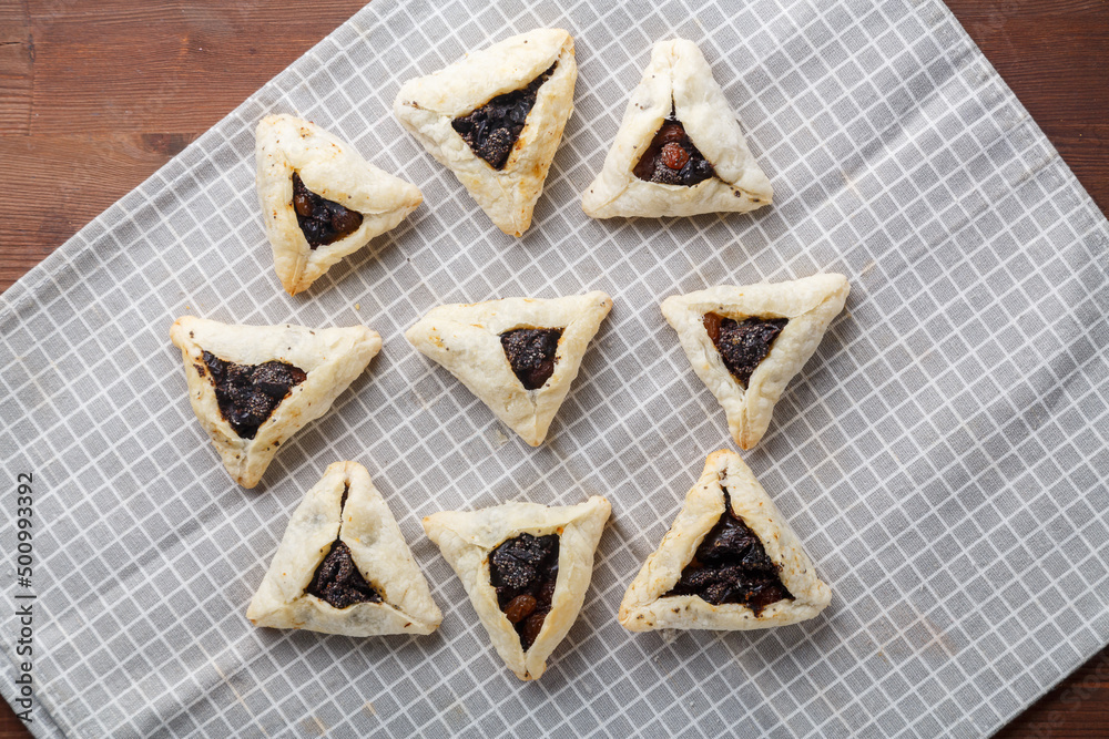Gomentashash with poppy seeds and prunes freshly baked for the holiday of Purim on a gray checkered towel. Gomentashash with poppy seeds and prunes freshly baked for the holiday of Purim on a gray checkered towel.