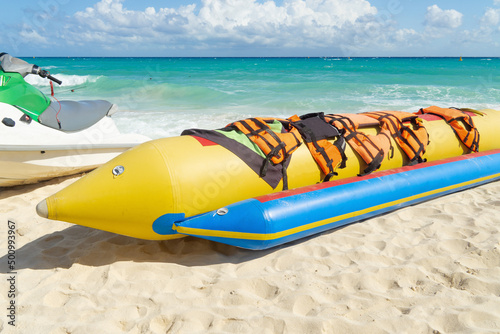 Inflatable bananas for group skating on the sea. Active rest,  attraction on the water. Banana boat with life jackets on a sandy beach against the backdrop of the sea.