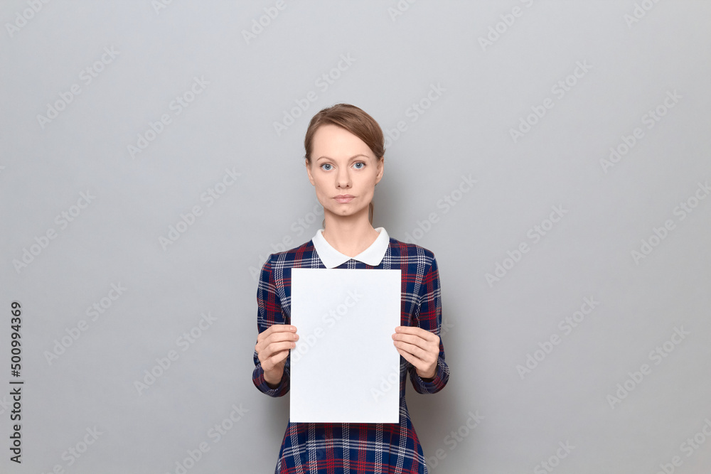 Studio portrait of serious young woman holding white blank paper sheet Studio portrait of serious young woman holding white blank paper sheet