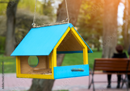 Wooden blue and yellow birdhouse on a rope in the farm park zone. Shelter for bird breeding, nesting box on a tree. Food box for starving animals. photo