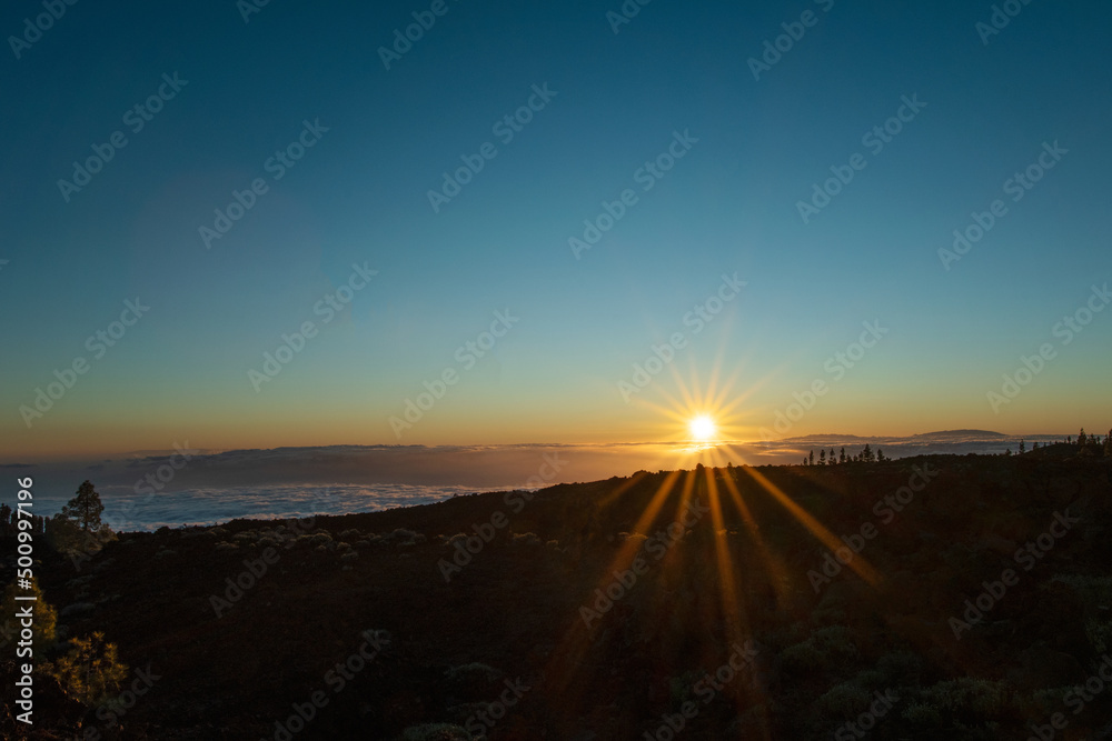 Beautiful sunset over the volcanic landscape and nature up in the mountain. Golden hour and sunlight above the clouds.  Photo taken at Teide national park in Tenerife, Spain.