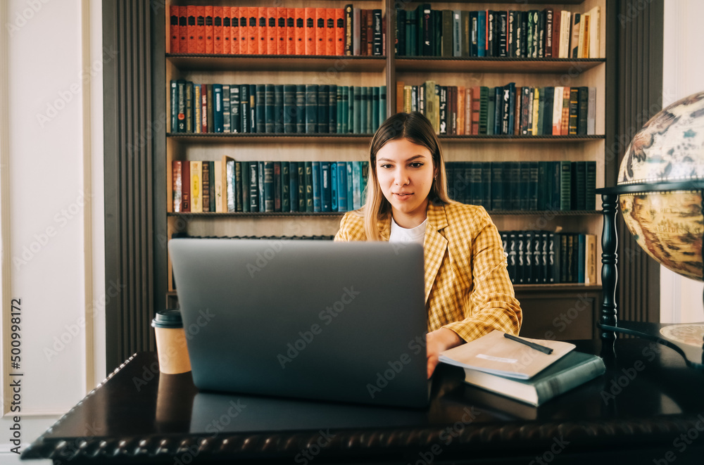 Portrait of young woman college student studying with laptop, preparing for test exam, writing essay doing homework in the library. Portrait of young woman college student studying with laptop, preparing for test exam, writing essay doing homework in the library.