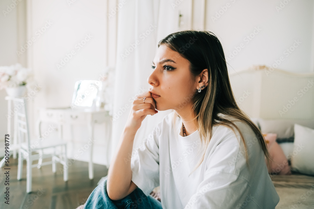 Young bored millennial woman sitting on a bed alone at home. Fatigue or emotionally exhausted concept