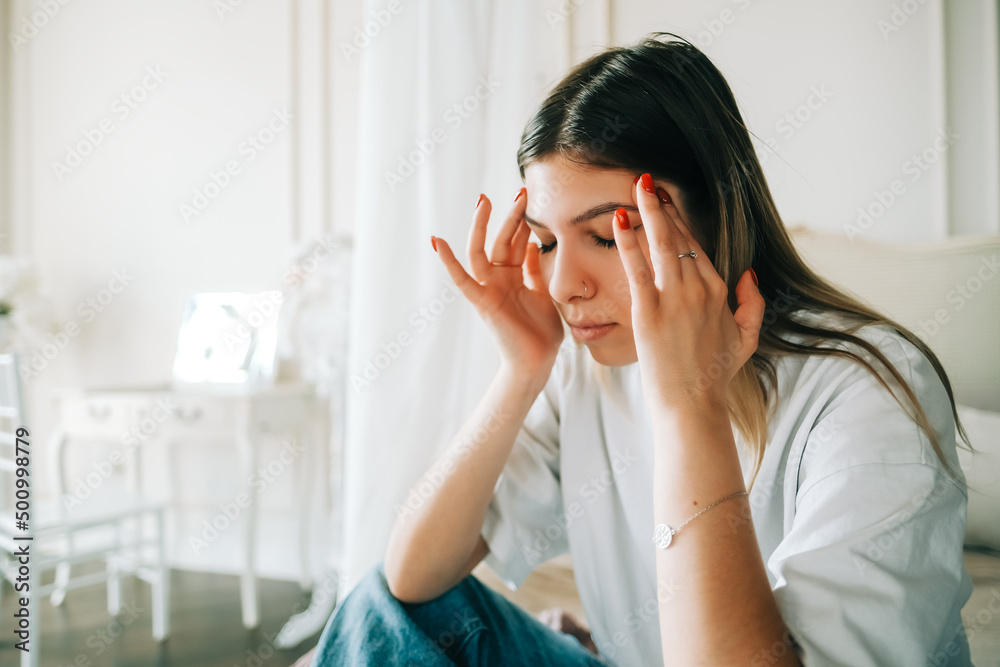 Young bored millennial woman sitting on a bed alone at home. Fatigue or emotionally exhausted concept Young bored millennial woman sitting on a bed alone at home. Fatigue or emotionally exhausted concept