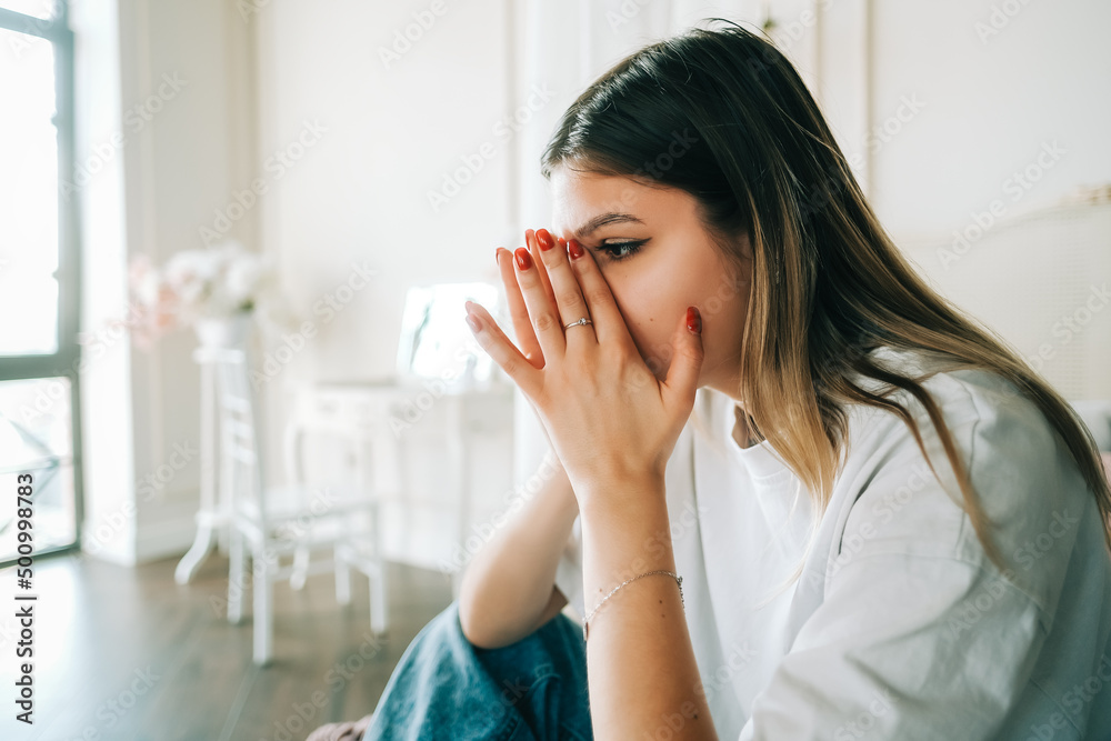 Young bored millennial woman sitting on a bed alone at home. Fatigue or emotionally exhausted concept Young bored millennial woman sitting on a bed alone at home. Fatigue or emotionally exhausted concept