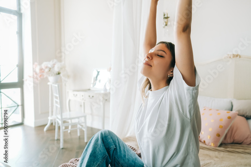 Attractive caucasian young woman in doing stretching exercise sitting on a bed and enjoying sunny morning.
