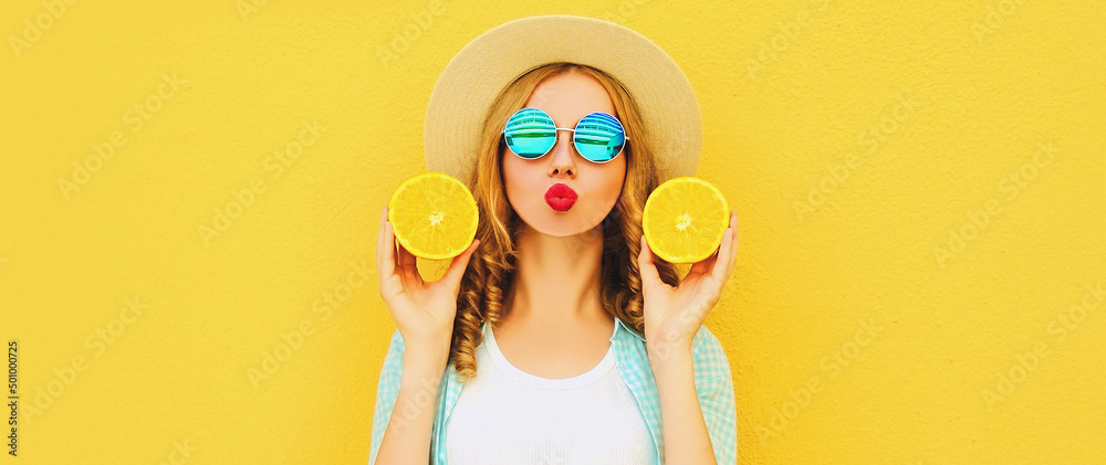 Summer portrait of happy young woman blowing her lips with slices of fresh orange fruits wearing straw hat, sunglasses on yellow background Summer portrait of happy young woman blowing her lips with slices of fresh orange fruits wearing straw hat, sunglasses on yellow background