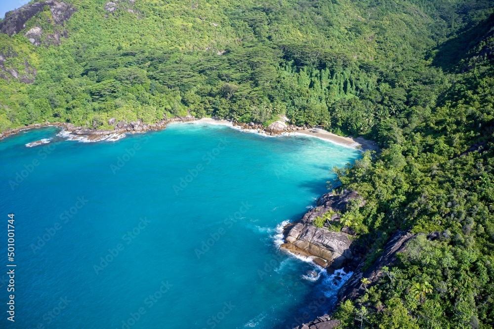 Fototapeta premium Drone field of view of secret cove with turquoise blue water meeting the forest on secluded island of Mahe, Seychelles.
