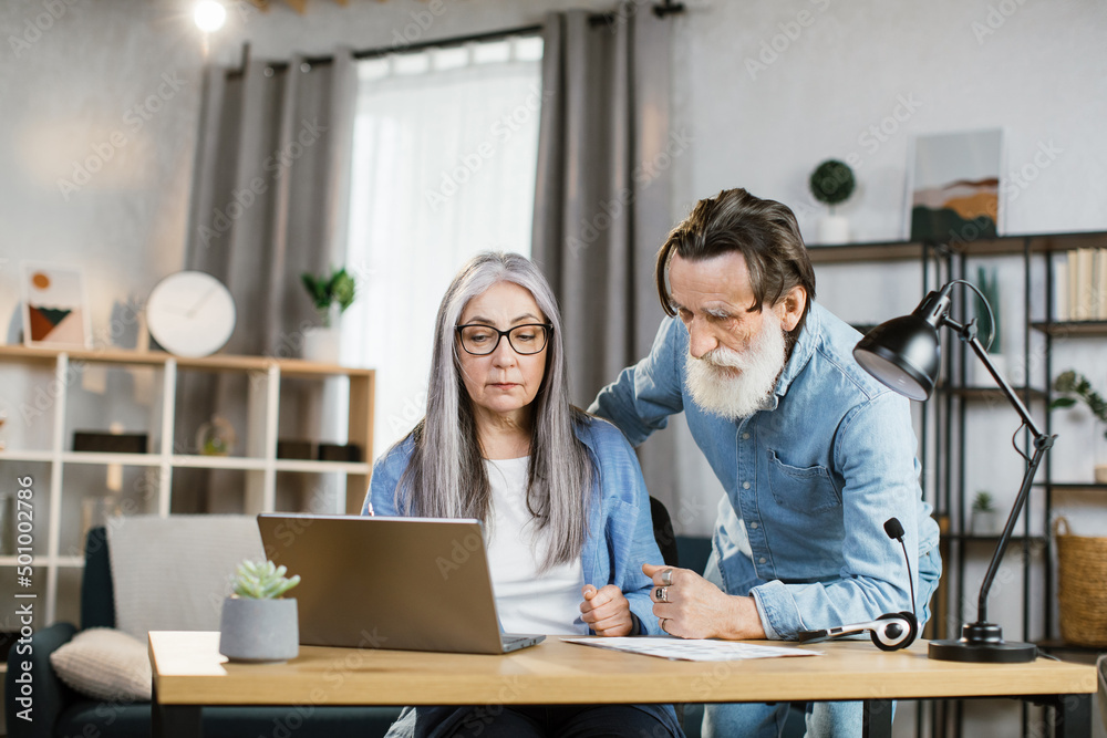 Obraz premium Senior caucasian man and woman in casual outfit looking at computer screen during working meeting. Mature business partners cooperating at bright office.