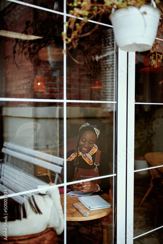 View through the window on young hipster african american woman studying in the internet cafe.