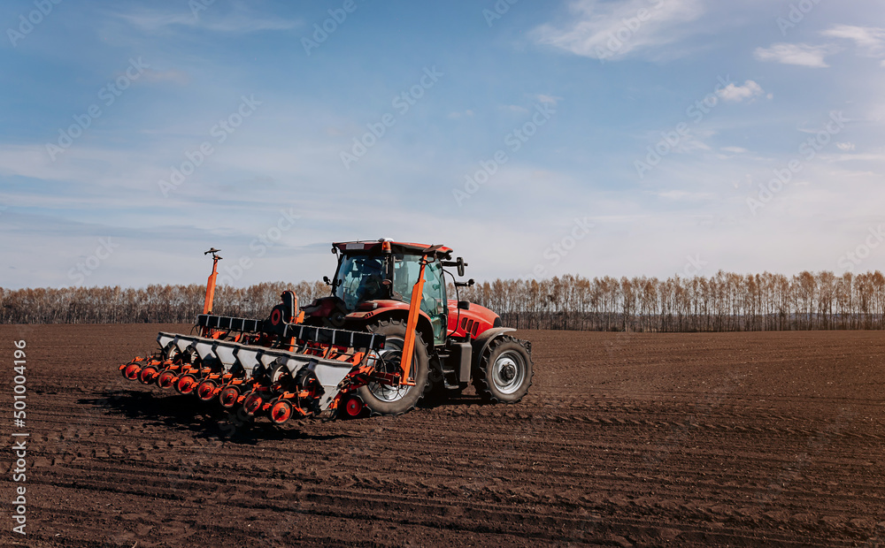 Obraz premium Spring sowing season. Farmer with a tractor sows corn seeds on his field. Planting corn with trailed planter. Farming seeding. The concept of agriculture and agricultural machinery.