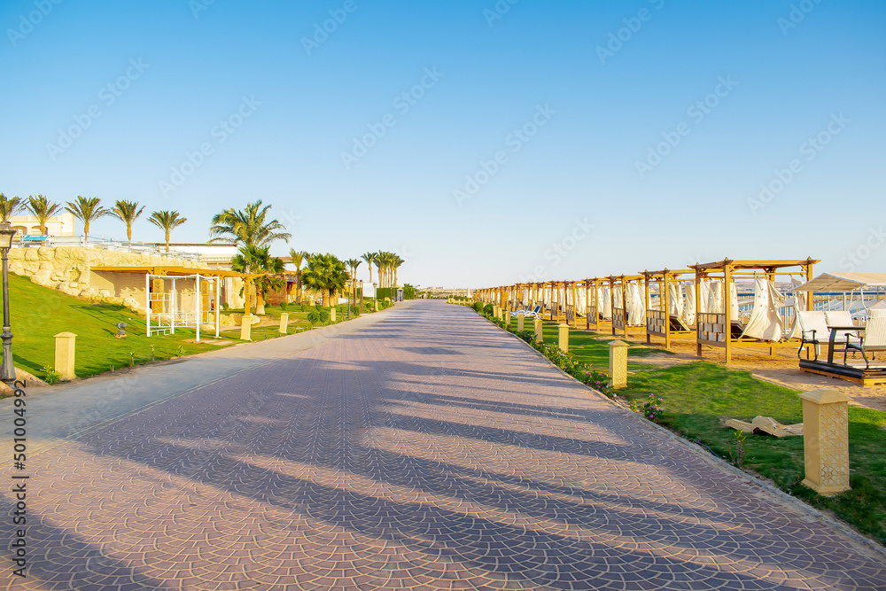 Road along lots of wooden furniture for rest, deck chair bed, gazebo on sand beach with curtains, tropical sea luxury resort.Summer vacation on warm sunny day outdoor in sunshine, sunlight