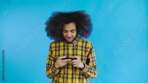 A young man with an African hairstyle on a blue background is playing on the phone. On a colored background