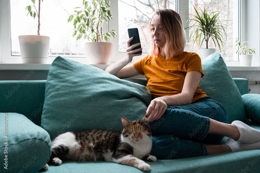 Young woman in yellow t-shirt sitting on sofa with cat holdind smartphone. Young woman in yellow t-shirt sitting on sofa with cat holdind smartphone.