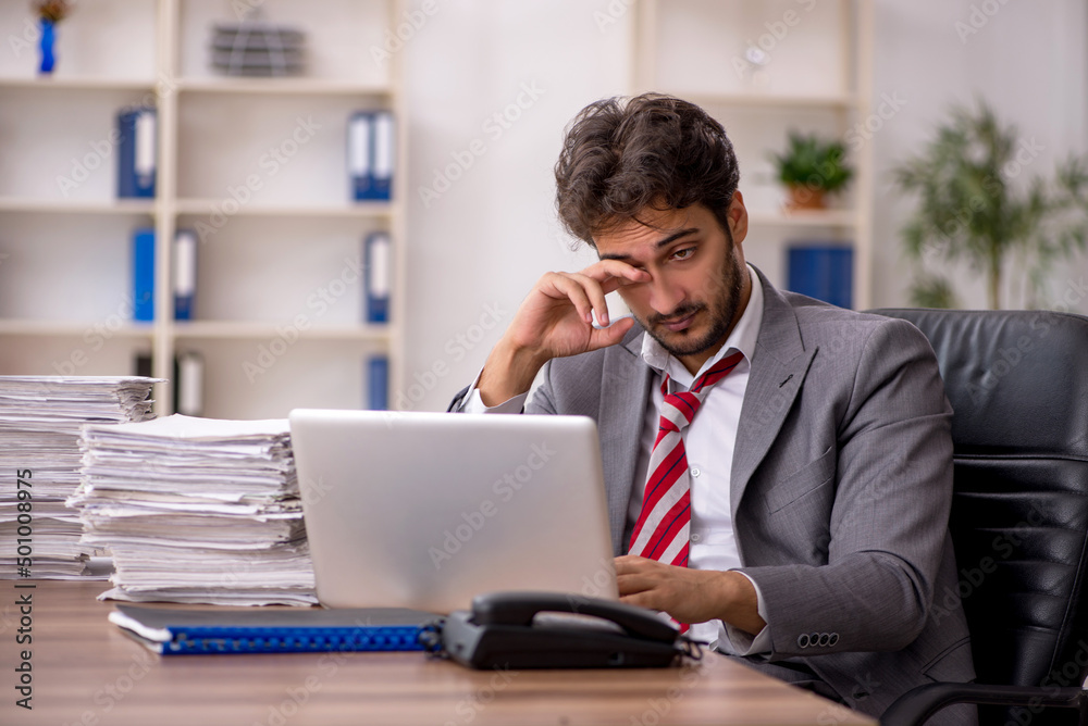 Young male employee unhappy with excessive work in the office Young male employee unhappy with excessive work in the office