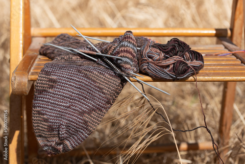 A half-finished sock lies on a brown old wooden folding chair. The chair is outdoors on a dry meadow