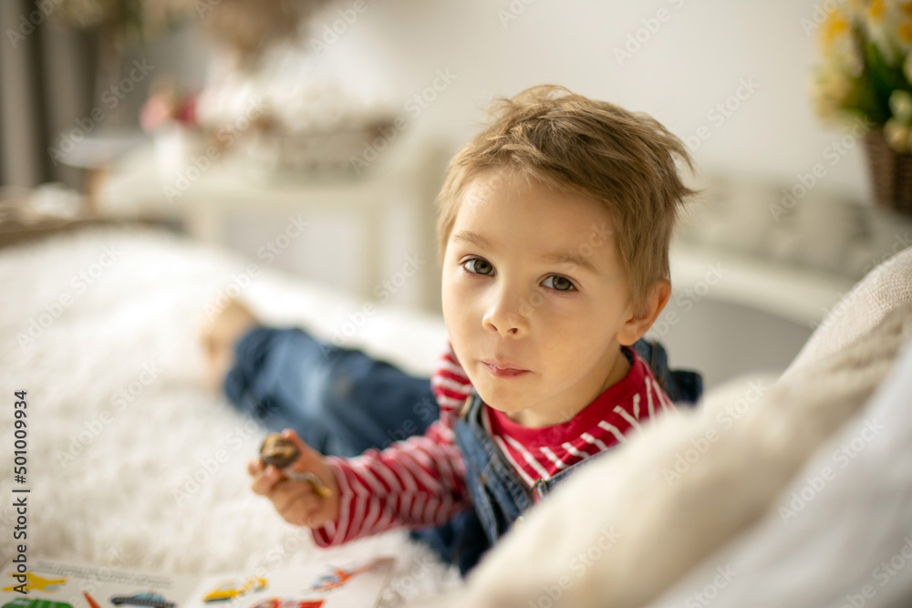 Cute child at home with little newborn chicks, eating chocolate candy in bed Cute child at home with little newborn chicks, eating chocolate candy in bed