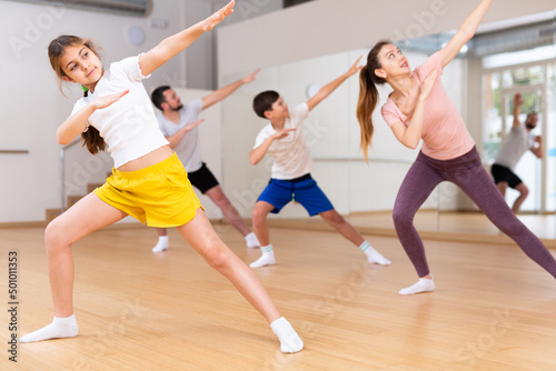 Portrait of happy preteen girl practicing dynamic synchronous choreography with her family in modern dance studio..