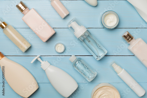 Different cosmetic bottles and container on wooden background, top view