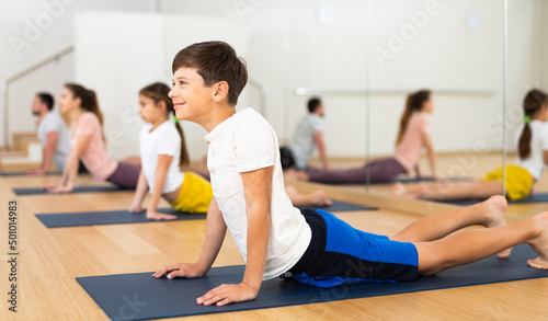 Young boy doing cobra pose during family group training in gym.