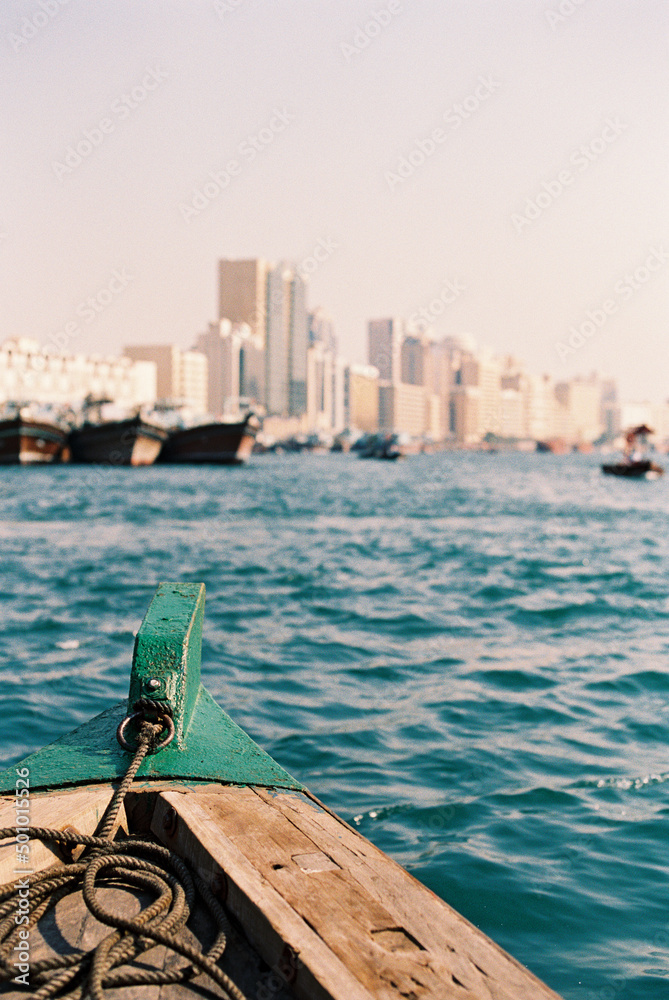 detail of bow of wooden boat in Dubai with city views in distance