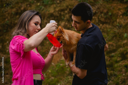 Woman giving water to her pet dog in a red container, while a man holds the animal.