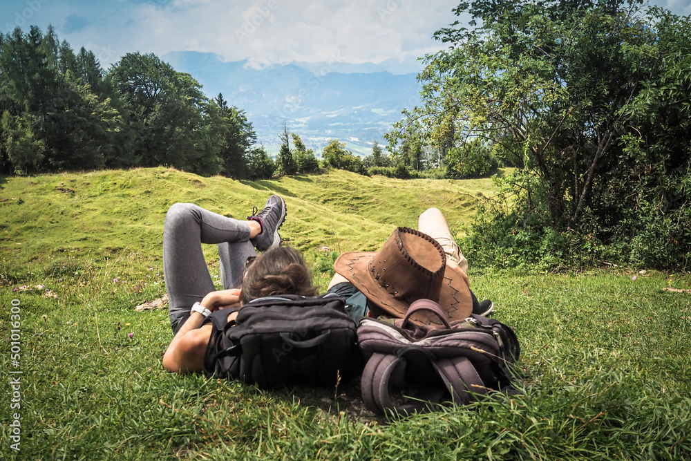 romantic sportive couple lying in the green grass on the mountain top enjoying the view of nature forest after a strenuous hike with their backpacks romantic sportive couple lying in the green grass on the mountain top enjoying the view of nature forest after a strenuous hike with their backpacks