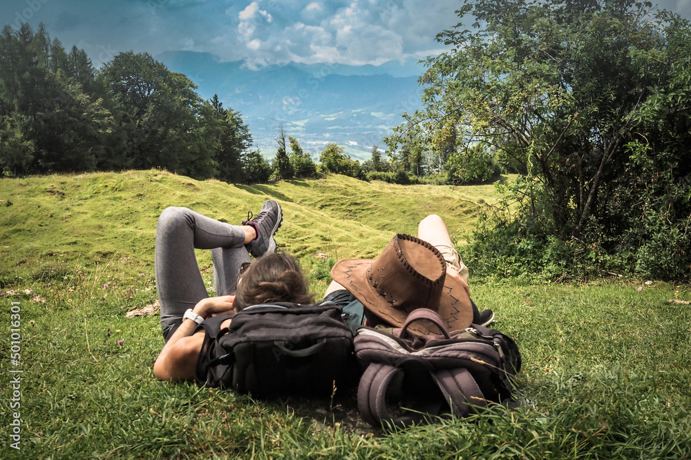 romantic sportive couple lying in the green grass on the mountain top enjoying the view of nature forest after a strenuous hike with their backpacks romantic sportive couple lying in the green grass on the mountain top enjoying the view of nature forest after a strenuous hike with their backpacks