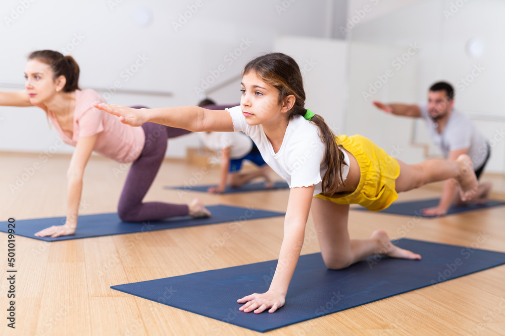 Positive pre-teen girl performing yoga exercises with brother and parents at gym, family health concept
