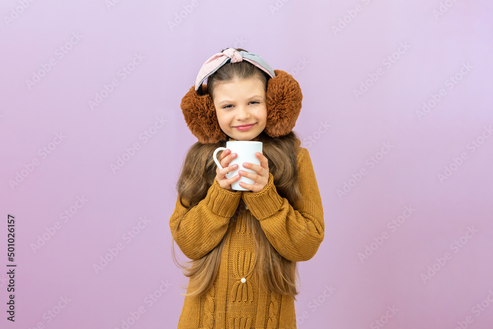A child with warm headphones on his head drinks a warming drink in the cold season. A child with warm headphones on his head drinks a warming drink in the cold season.