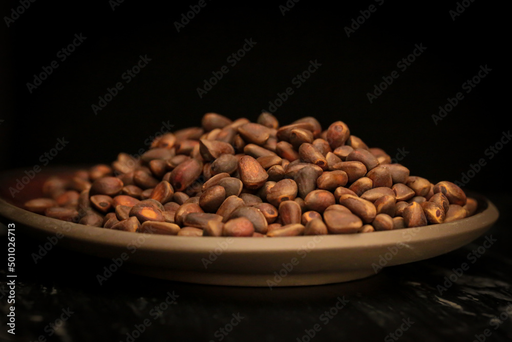 Pine nuts on a plate on a black background.Nuts and seeds. Healthy food and snacks.Unpeeled pine nuts close-up in a ceramic bowl on a black marble background. Pine nuts on a plate on a black background.Nuts and seeds. Healthy food and snacks.Unpeeled pine nuts close-up in a ceramic bowl on a black marble background.
