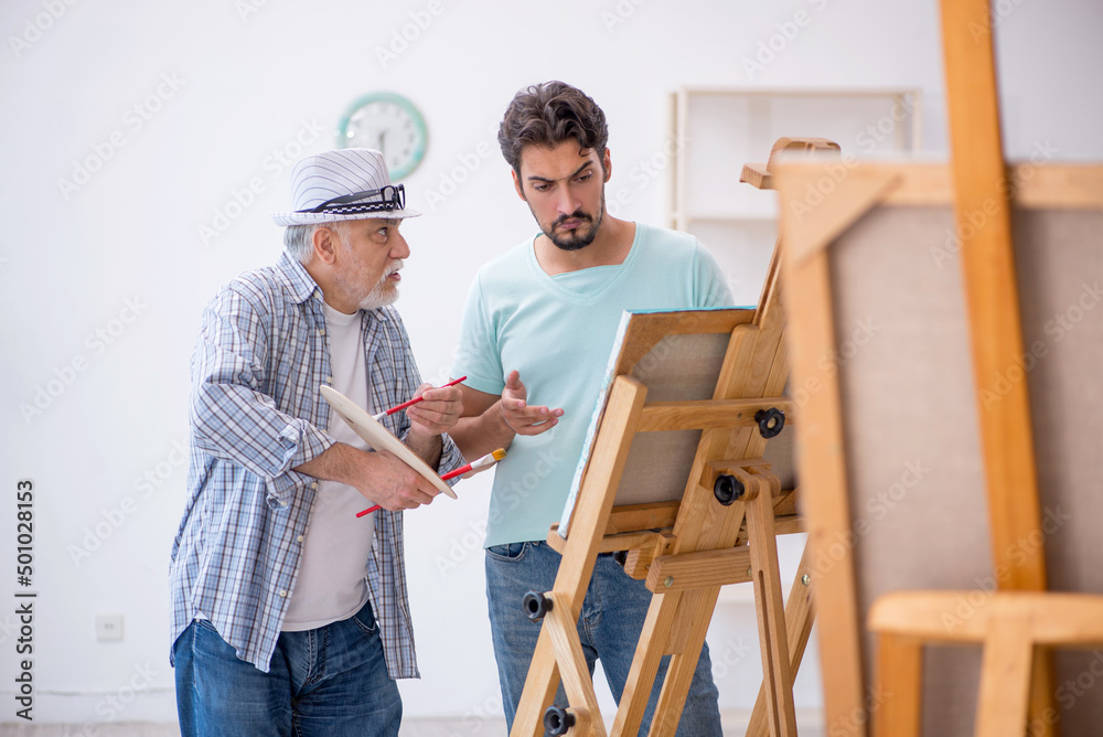 Old painter teaching young student at studio