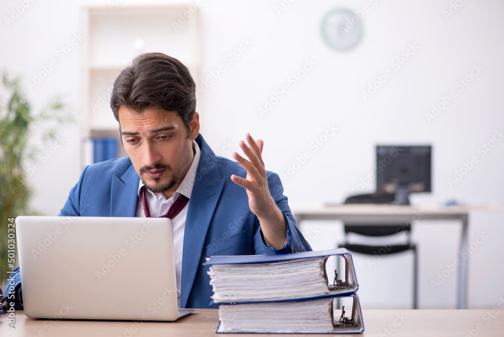 Young male employee unhappy with excessive work in the office Young male employee unhappy with excessive work in the office