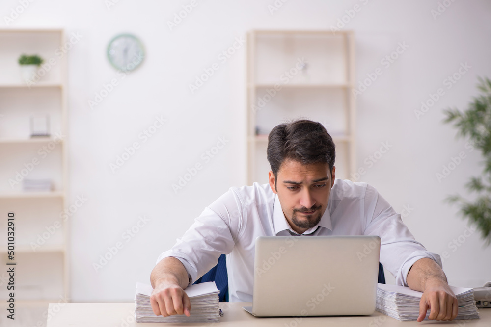 Young male employee unhappy with excessive work in the office Young male employee unhappy with excessive work in the office