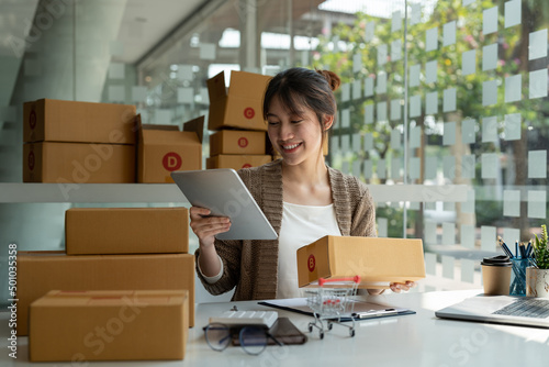 Sell online, Young asian woman checking order and customer's details and addresses on laptop or box in order to prepare for shipping according to the information, Online shopping SME entrepreneur