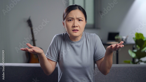 Asian woman feel confused shrugging and sitting in living room at home.