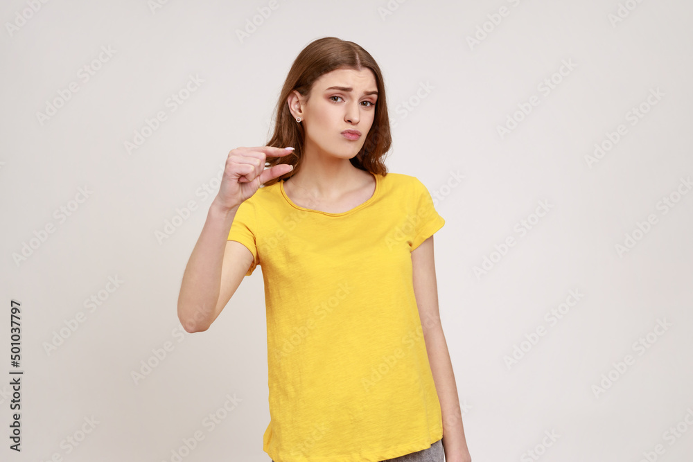 Please, some more. Portrait of cute teen girl in yellow T-shirt showing small size or little bit gesture with fingers, looking with imploring grimace. Indoor studio shot isolated on gray background. Please, some more. Portrait of cute teen girl in yellow T-shirt showing small size or little bit gesture with fingers, looking with imploring grimace. Indoor studio shot isolated on gray background.