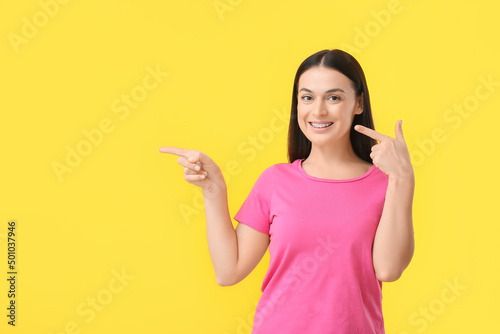 Beautiful woman with dental braces pointing at something on yellow background