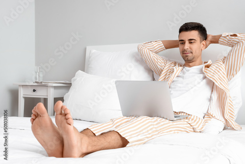 Young barefooted man using laptop in bedroom