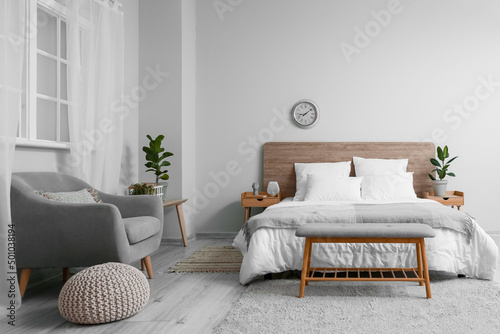 Interior of bedroom with comfortable bed and stylish clock on light wall