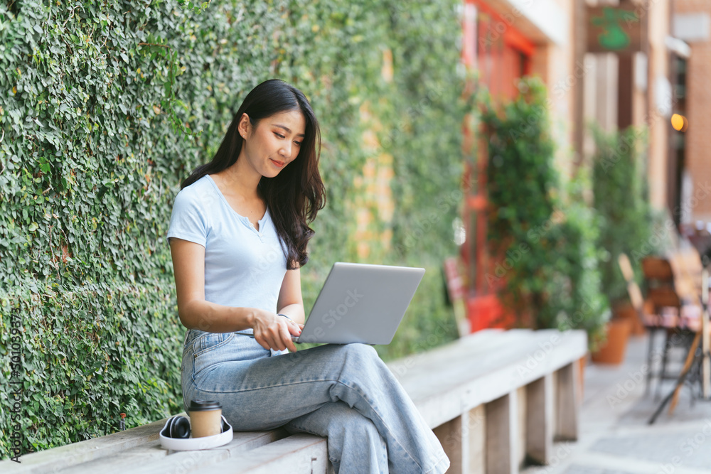 Portrait of beautiful Asian woman sitting outdoors at coffee shop restaurant during summer, using smart wireless technology computer laptop and smartphone, relaxing coffee break at cafe restaurant. Portrait of beautiful Asian woman sitting outdoors at coffee shop restaurant during summer, using smart wireless technology computer laptop and smartphone, relaxing coffee break at cafe restaurant.