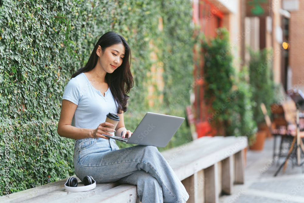 Portrait of beautiful Asian woman sitting outdoors at coffee shop restaurant during summer, using smart wireless technology computer laptop and smartphone, relaxing coffee break at cafe restaurant. Portrait of beautiful Asian woman sitting outdoors at coffee shop restaurant during summer, using smart wireless technology computer laptop and smartphone, relaxing coffee break at cafe restaurant.