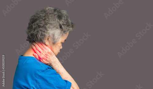 Senior woman suffering neck pain while standing against a gray background. Cervical dystonia disease. photo