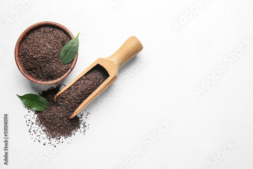 Bowl and scoop with dry tea leaves on white background, top view