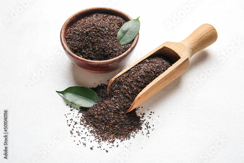 Bowl and scoop with dry tea leaves on white background